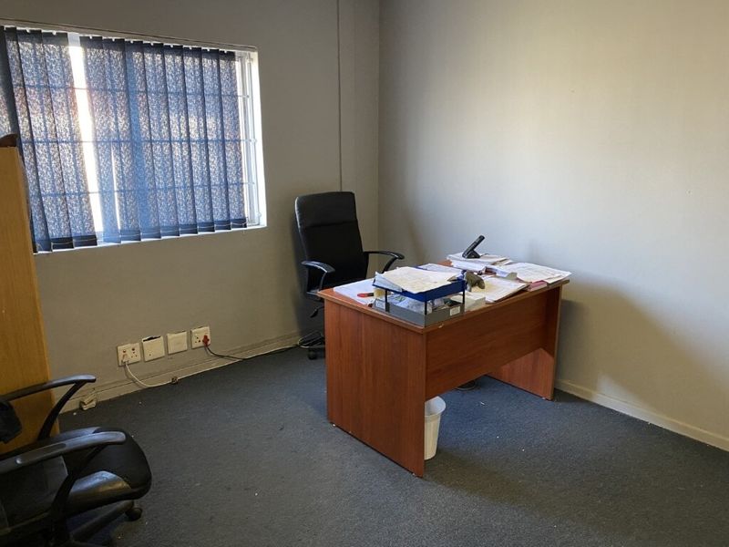 A functional office space featuring carpeted flooring, vertical blinds with security bars, and multiple electrical outlets for workspace connectivity.