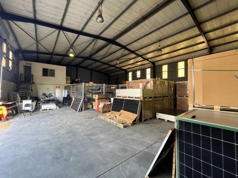Spacious industrial warehouse unit featuring high exposed steel roof trusses, durable concrete flooring, and a mezzanine access staircase.