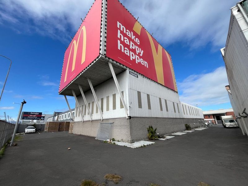 Industrial property featuring a large prominent billboard structure, corrugated metal cladding, and a paved asphalt yard area.