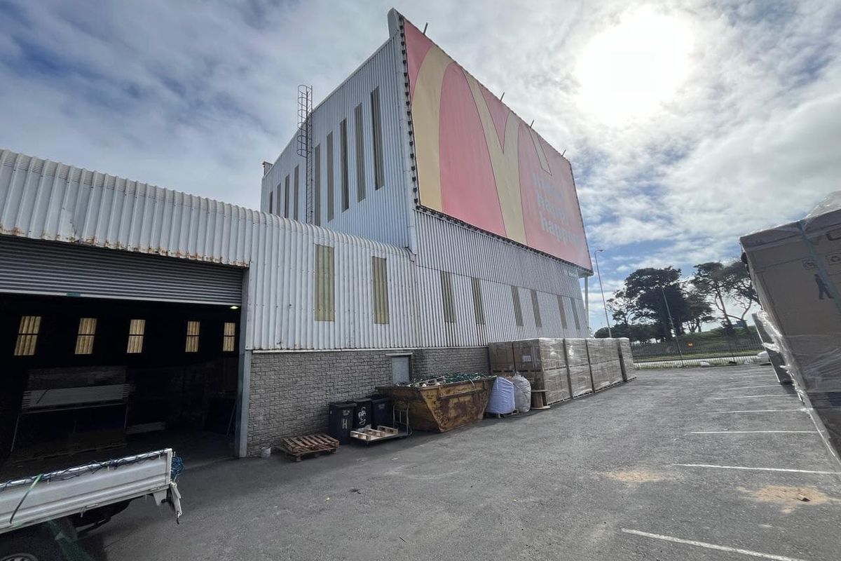 Rear exterior view of an industrial property featuring corrugated metal cladding, a large roller shutter door, and a prominent billboard advertisement.