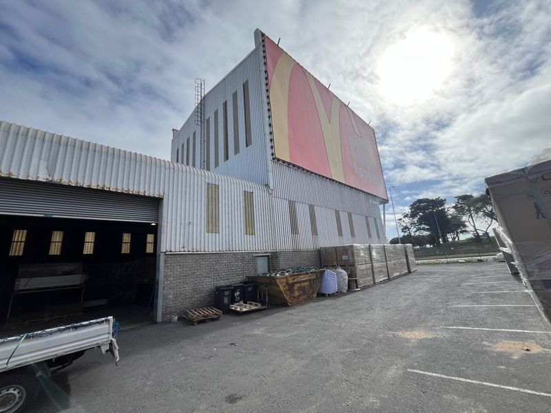 Rear exterior view of an industrial property featuring corrugated metal cladding, a large roller shutter door, and a prominent billboard advertisement.