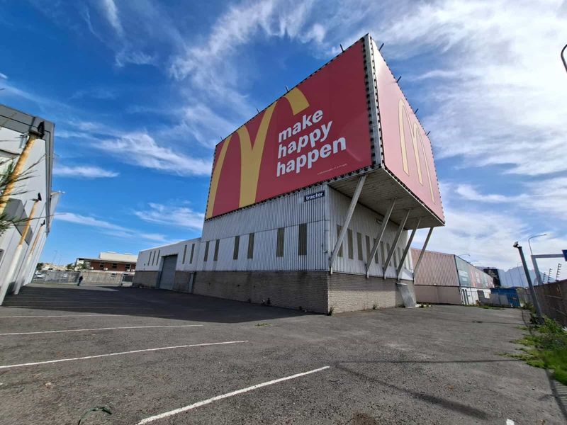 Industrial property featuring a large prominent advertising billboard, corrugated metal exterior cladding, and an expansive asphalt parking area.