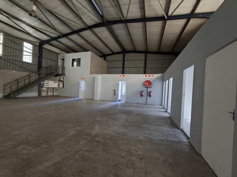 Spacious industrial warehouse area featuring high ceilings, concrete flooring, a mezzanine level with staircase access, and integrated fire safety equipment.