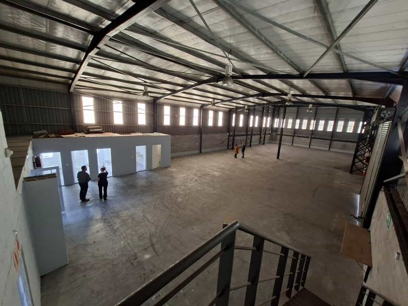 Spacious industrial warehouse featuring high ceilings with exposed steel trusses, concrete flooring, and a mezzanine level, suitable for various commercial or storage operations.