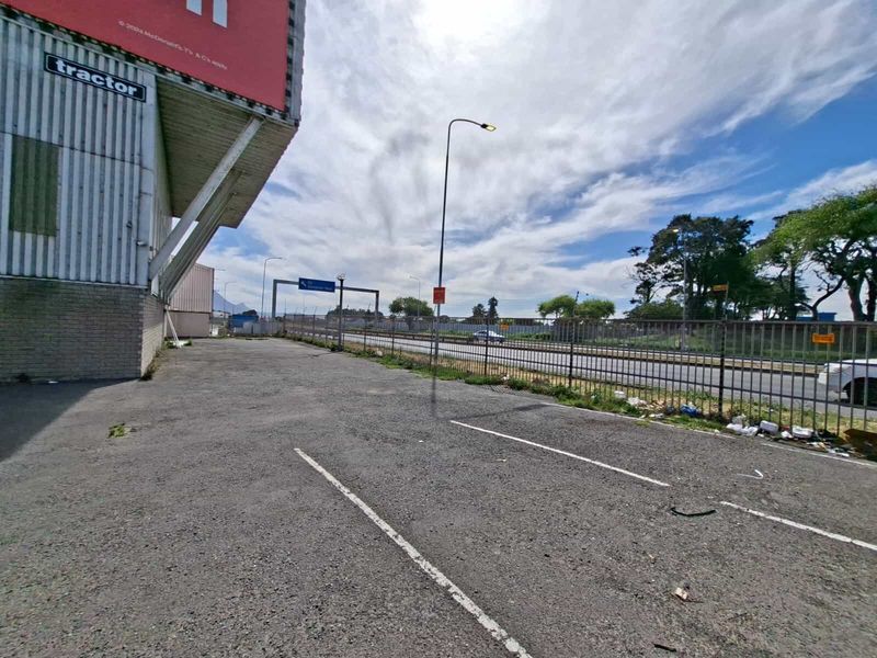 Exterior view of the industrial property featuring an asphalt parking area, metal perimeter fencing, and corrugated metal building cladding adjacent to a main road.