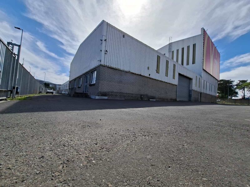 Industrial property exterior featuring corrugated metal cladding, a brick masonry base, and a large roller shutter door with an expansive asphalt driveway.