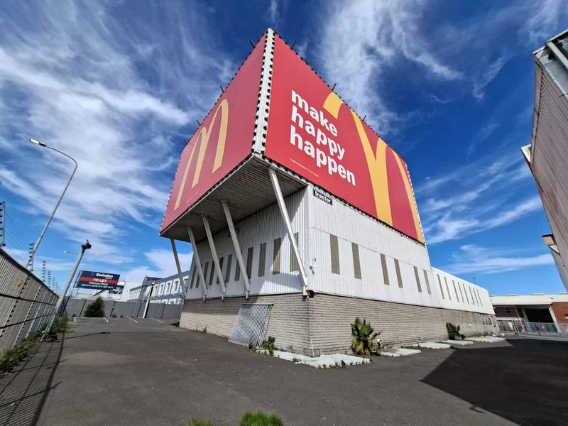 Industrial property exterior featuring a prominent large-scale billboard structure, corrugated metal siding, and a paved driveway area.