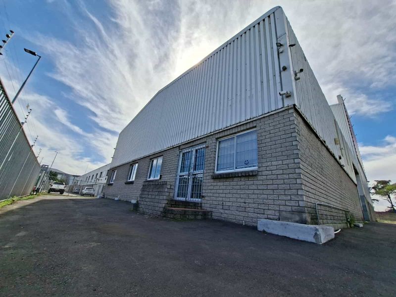 Exterior view of an industrial warehouse building featuring corrugated metal cladding, brick masonry, and secure gated access.