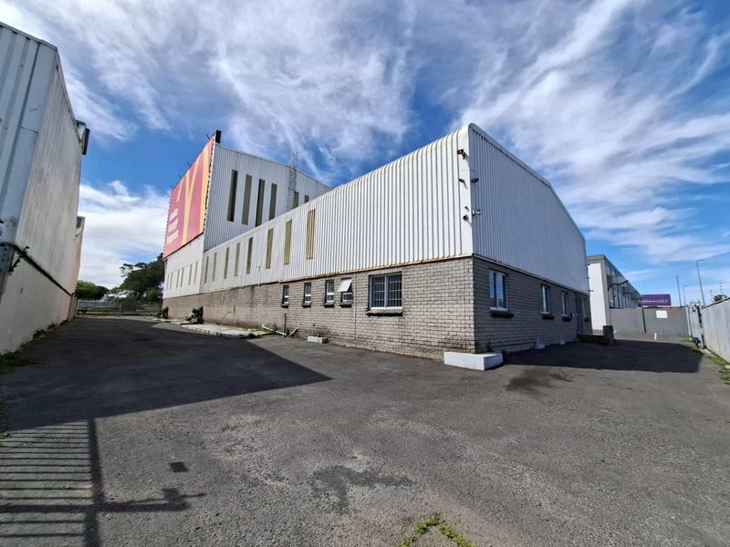 Rear exterior view of an industrial property featuring corrugated metal cladding, brick masonry base, and an asphalt yard area with a large billboard.