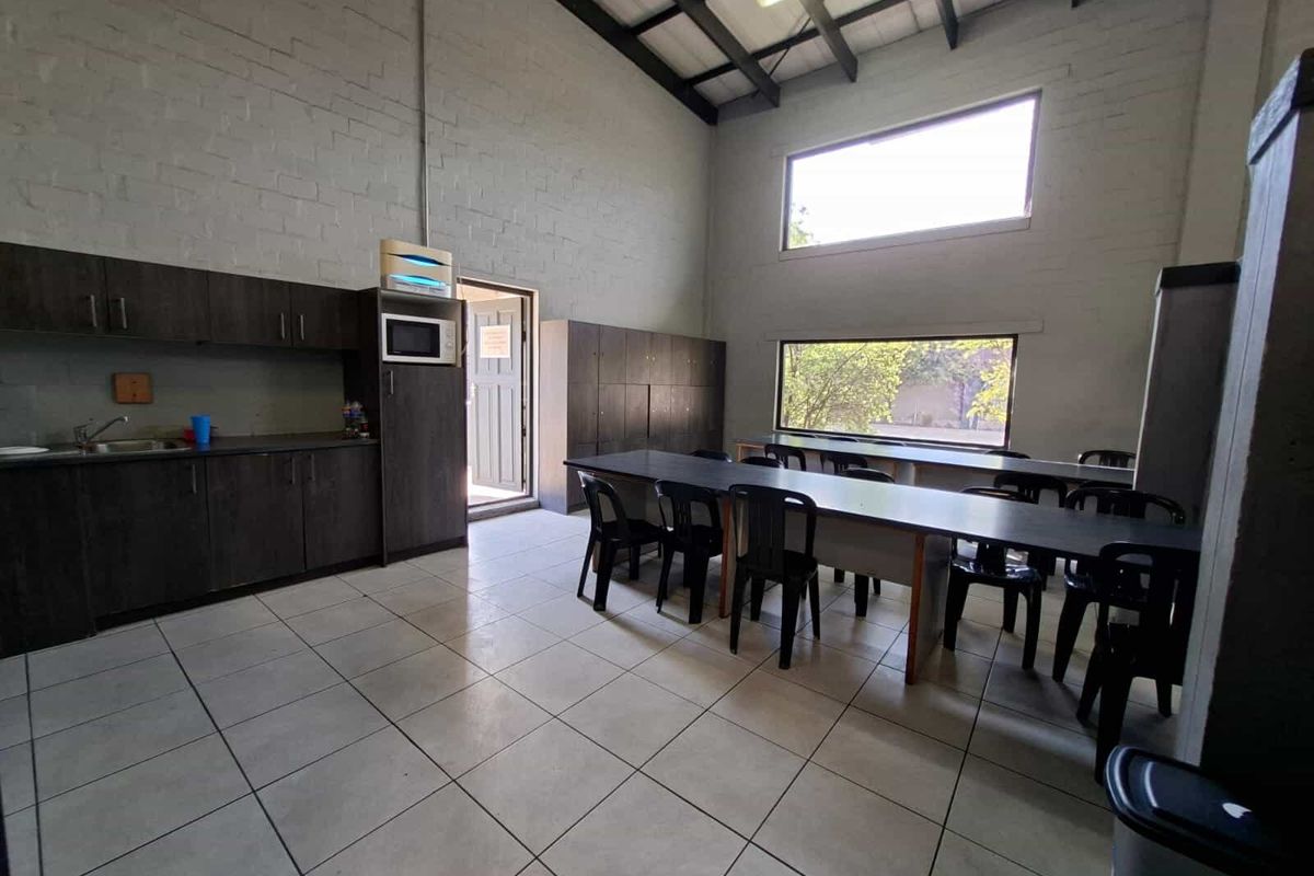 Industrial kitchen and break room featuring tiled floors, built-in cabinetry, exposed roof trusses, and large windows providing natural light.