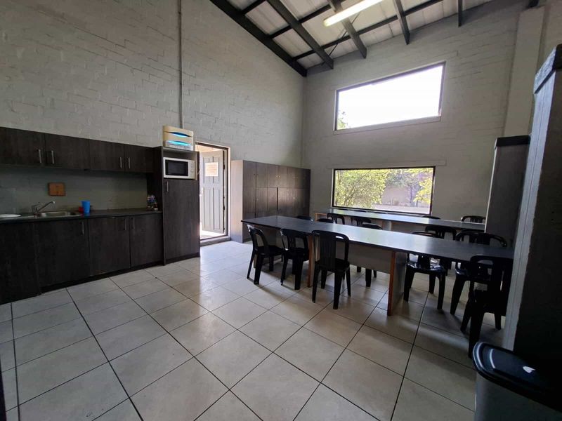 Industrial kitchen and break room featuring tiled floors, built-in cabinetry, exposed roof trusses, and large windows providing natural light.