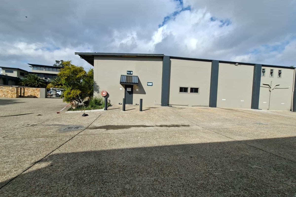 Exterior view of an industrial property featuring a concrete driveway, entrance door with awning, and bollards.