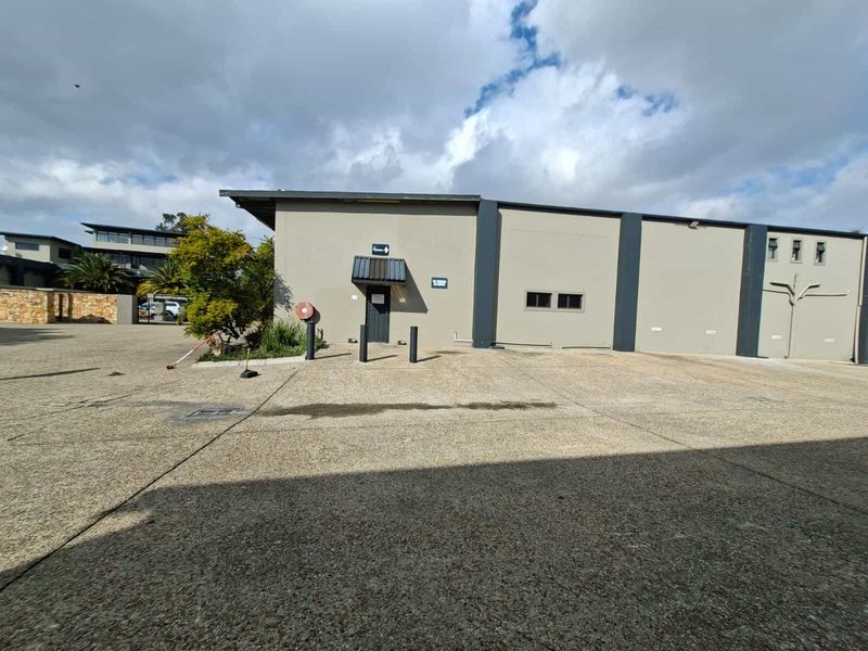Exterior view of an industrial property featuring a concrete driveway, entrance door with awning, and bollards.