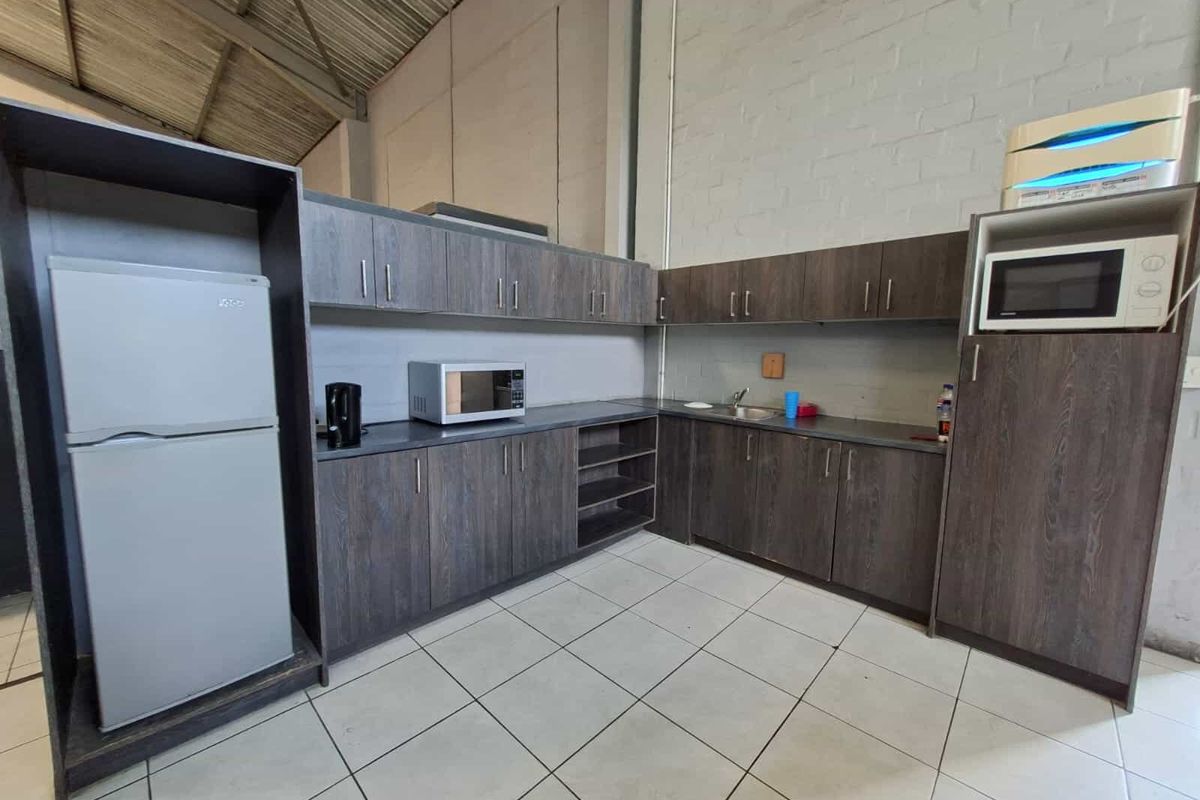 Industrial-style kitchenette featuring dark wood-grain cabinetry, laminate countertops, a stainless steel sink, and durable ceramic floor tiles under an exposed high ceiling.