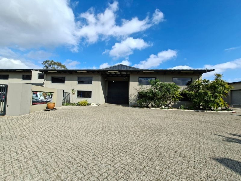 Front exterior view of an industrial property featuring a large roller shutter door, paved driveway, and secure perimeter walling.