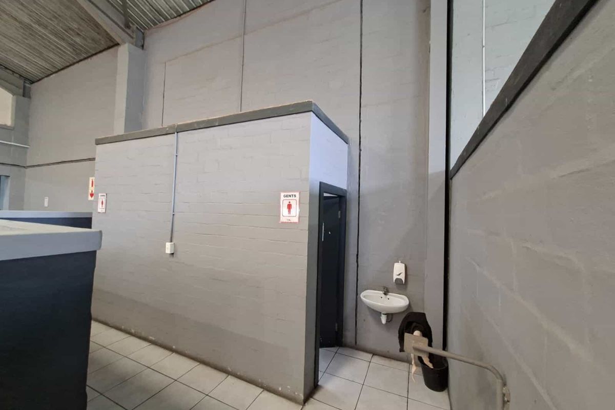 Industrial-style restroom facility featuring painted brick walls, tiled flooring, and a wall-mounted basin within an open-plan warehouse environment.