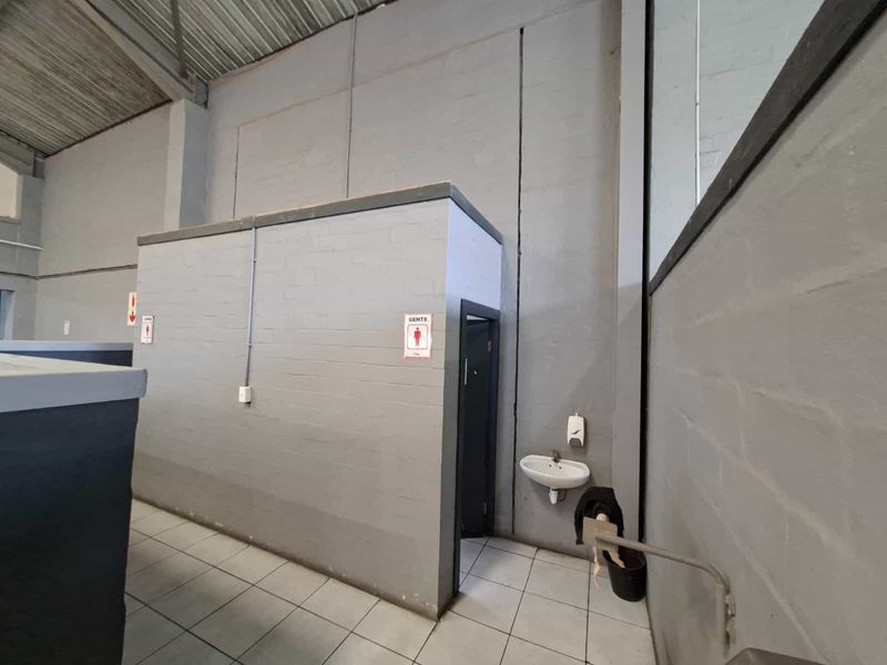 Industrial-style restroom facility featuring painted brick walls, tiled flooring, and a wall-mounted basin within an open-plan warehouse environment.