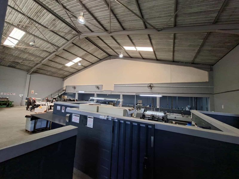 Spacious industrial warehouse featuring high exposed steel roof trusses, natural light from skylights, a mezzanine level, and partitioned operational work areas.