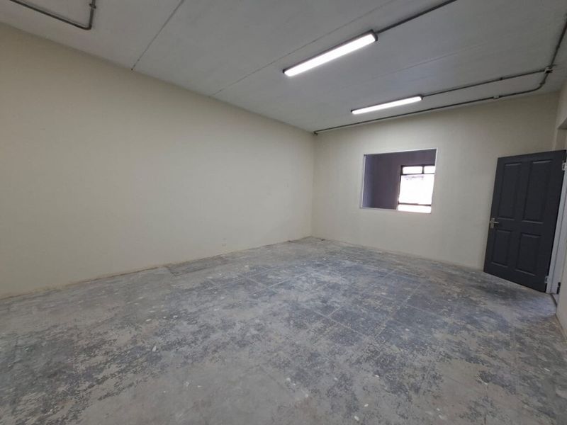An empty industrial utility space featuring concrete flooring, exposed conduit lighting, and a solid core door, suitable for storage or workshop use.