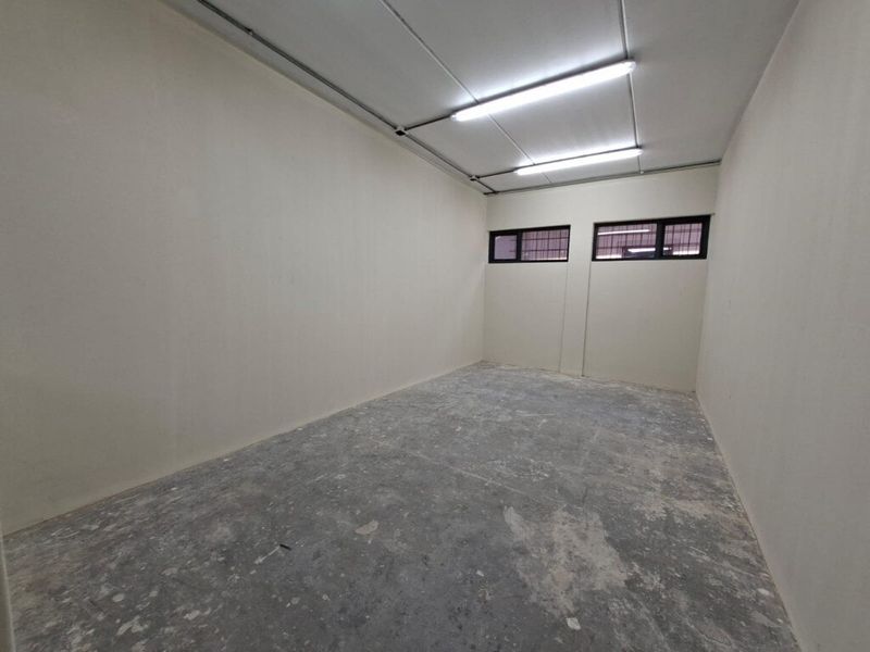 An empty, functional utility space featuring concrete flooring, high-level windows, and exposed fluorescent lighting, suitable for storage or workshop use.