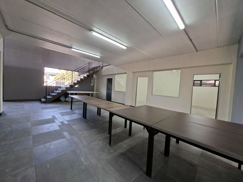 Spacious open-plan industrial area featuring tiled flooring, fluorescent lighting, and a metal staircase leading to an upper level.