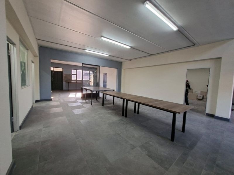 Spacious open-plan industrial area featuring tiled flooring, suspended ceilings, and bright fluorescent lighting, suitable for versatile office or workshop use.