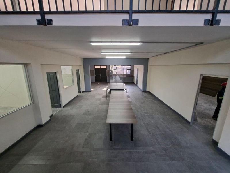 Spacious open-plan industrial office area featuring tiled flooring, mezzanine level with metal railing, and integrated internal glass partitions.