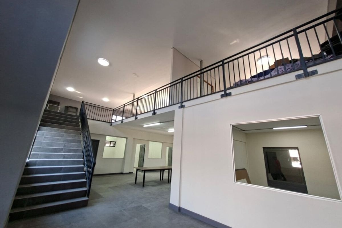 Spacious open-plan industrial interior featuring a staircase leading to a mezzanine level, tiled flooring, and large internal windows providing natural light.