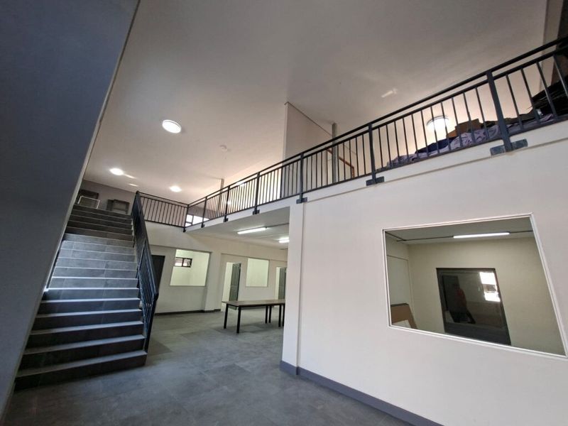 Spacious open-plan industrial interior featuring a staircase leading to a mezzanine level, tiled flooring, and large internal windows providing natural light.