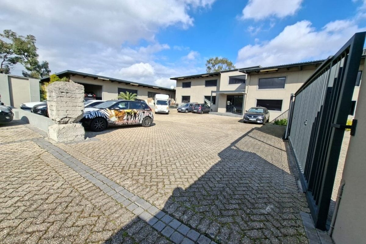 Front view of an industrial property featuring a paved courtyard, secure gated entrance, and multiple warehouse or office units with covered parking.