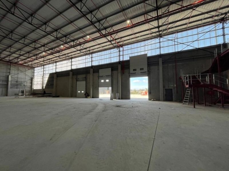 Spacious industrial warehouse featuring high ceilings with exposed steel trusses, concrete flooring, fire sprinkler system, and multiple roller shutter doors for easy access.
