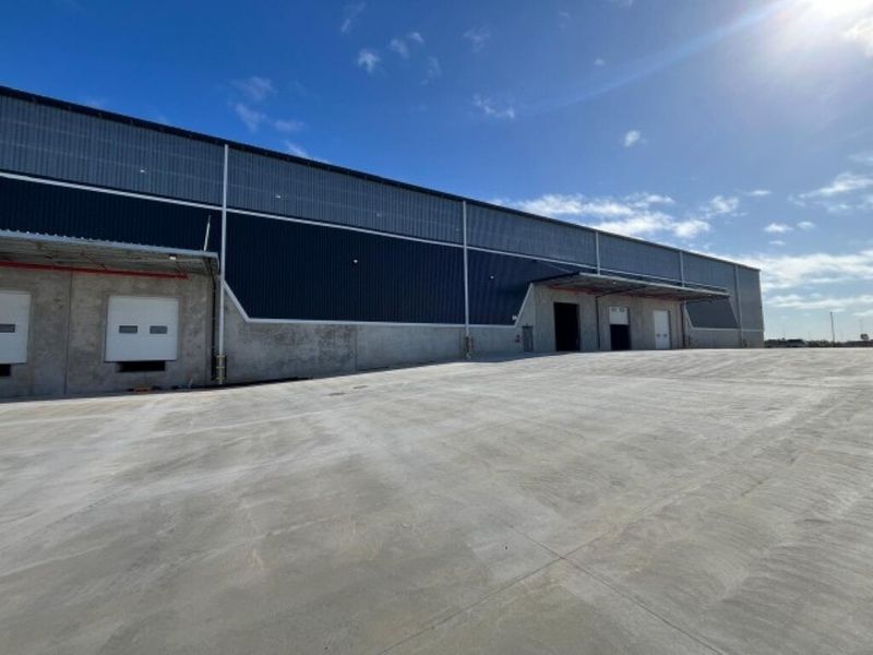 Industrial warehouse exterior featuring a large concrete yard, multiple loading docks with roller shutter doors, and modern metal cladding.