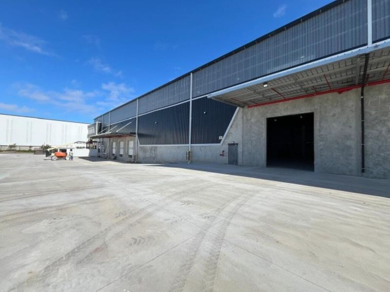 Industrial warehouse exterior featuring a large concrete hardstand, metal cladding, and a high-clearance roller shutter door with a loading bay canopy.