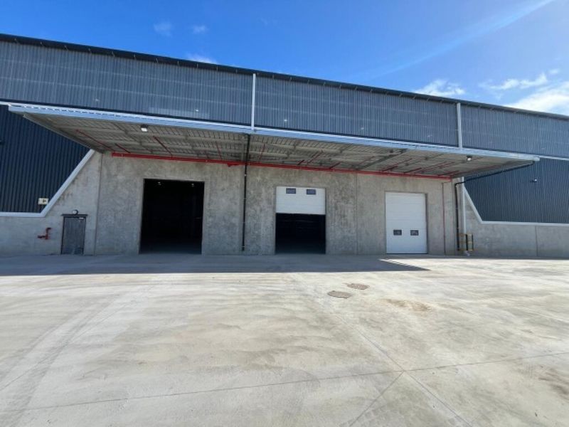 Industrial warehouse exterior featuring a large concrete yard, covered loading bay, and multiple roller shutter doors for efficient access.