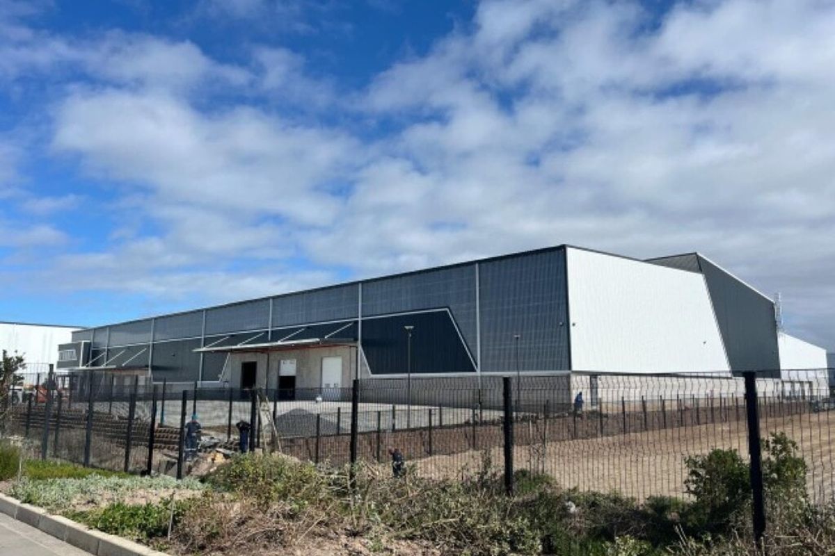 A modern industrial warehouse facility featuring metal cladding, secure perimeter fencing, and a functional loading bay area.