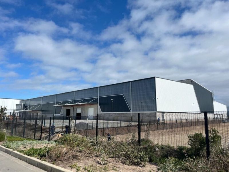 A modern industrial warehouse facility featuring metal cladding, secure perimeter fencing, and a functional loading bay area.