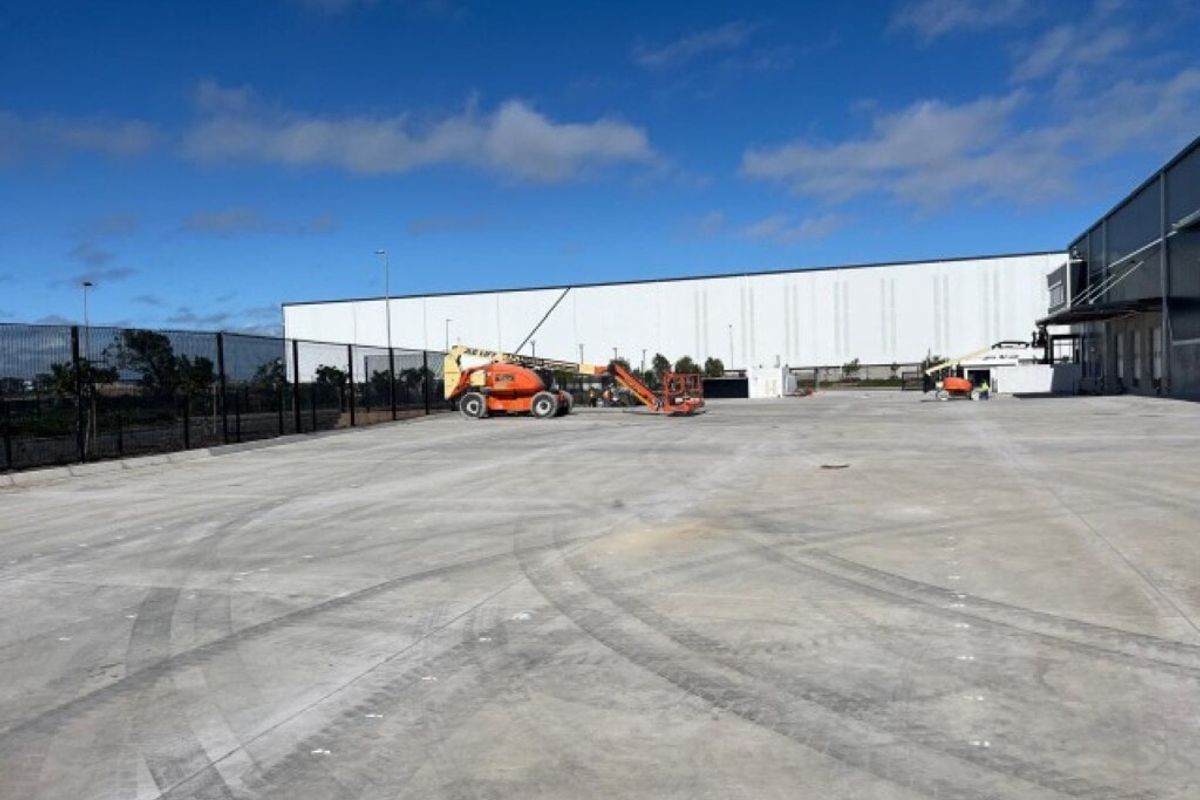 Expansive industrial concrete hardstand area with perimeter security fencing and access to the main warehouse facility.