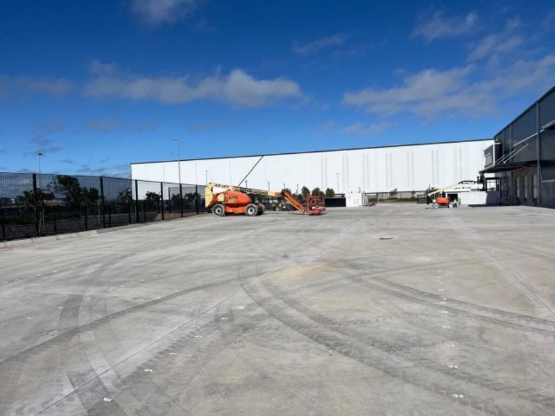 Expansive industrial concrete hardstand area with perimeter security fencing and access to the main warehouse facility.