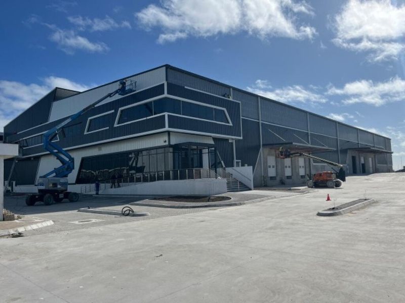Modern industrial warehouse facility featuring extensive metal cladding, large glass facade, and multiple loading docks with a spacious concrete yard.