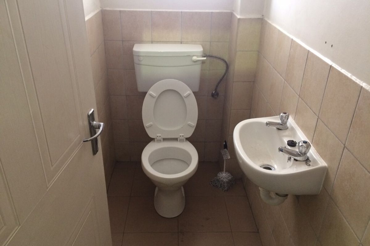 A compact industrial restroom featuring a standard toilet and wall-mounted basin with tiled walls and flooring.