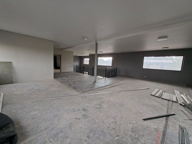 Spacious open-plan industrial interior featuring a metal staircase railing, large windows, and recessed lighting, currently in an unfinished state awaiting final flooring and finishes.