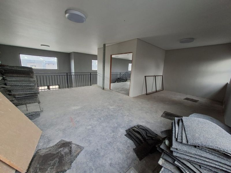 An open-plan industrial space featuring a metal balustrade, neutral wall finishes, and flush mount lighting, currently in an unfinished state.