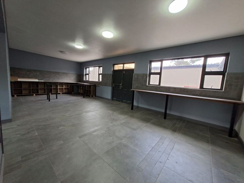 A spacious, well-lit utility or workshop area featuring durable tiled flooring, built-in shelving, and fixed workbenches, suitable for various industrial or commercial applications.