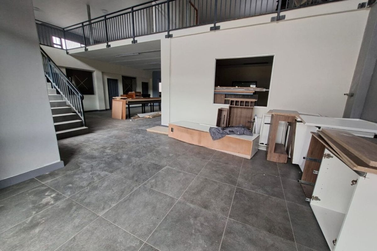 Spacious open-plan industrial area featuring a mezzanine level, metal staircase, and tiled flooring, currently undergoing fit-out with unfinished cabinetry.