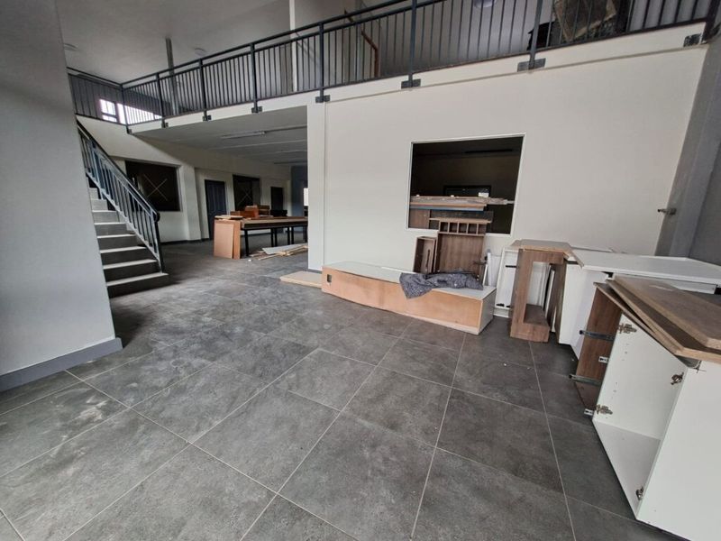 Spacious open-plan industrial area featuring a mezzanine level, metal staircase, and tiled flooring, currently undergoing fit-out with unfinished cabinetry.