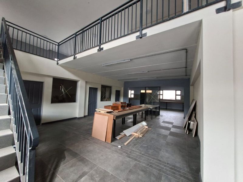 Spacious industrial open-plan area featuring a mezzanine level, metal staircase, tiled flooring, and ample natural light through internal windows.