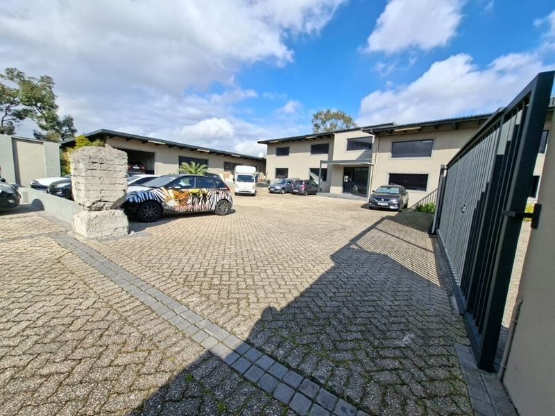 Front view of an industrial property featuring a paved courtyard, secure gated entrance, and multiple warehouse or office units with covered parking.