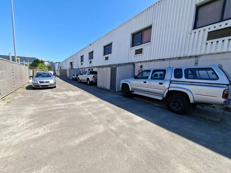 Rear exterior view of an industrial property featuring corrugated metal cladding, concrete driveway, and security fencing.