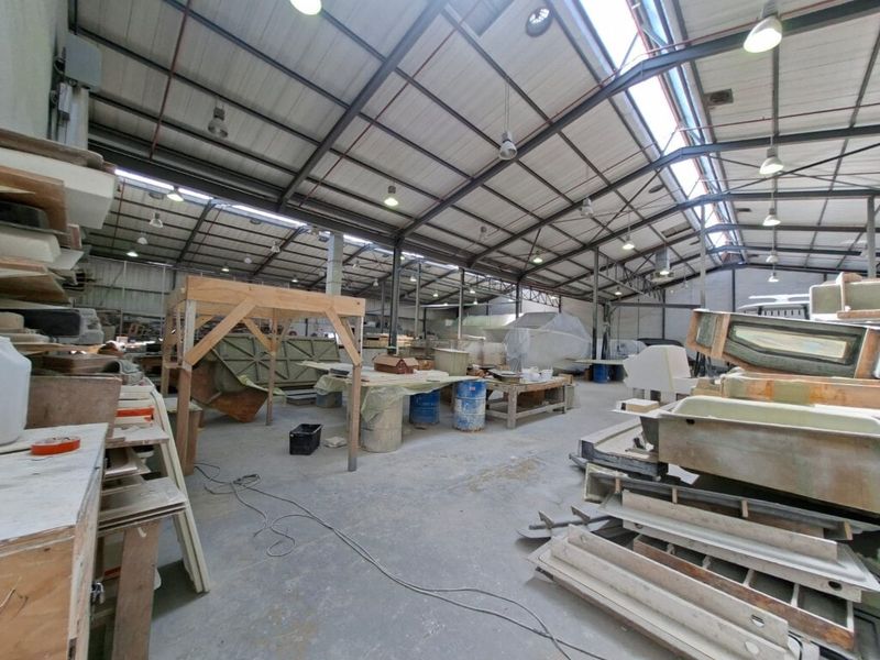 Spacious industrial workshop area featuring high ceilings with exposed steel trusses, integrated skylights, and durable concrete flooring, suitable for manufacturing or storage operations.