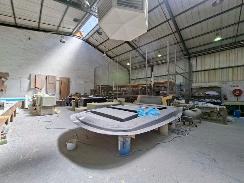 Spacious industrial utility area featuring high ceilings with exposed steel trusses, skylights, concrete flooring, and a secure chain-link partitioned storage section.